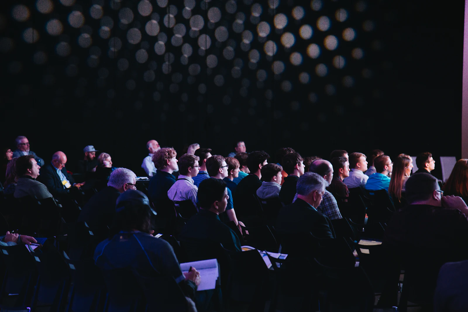 A conference audience seated in a dark hall, facing a lit stage