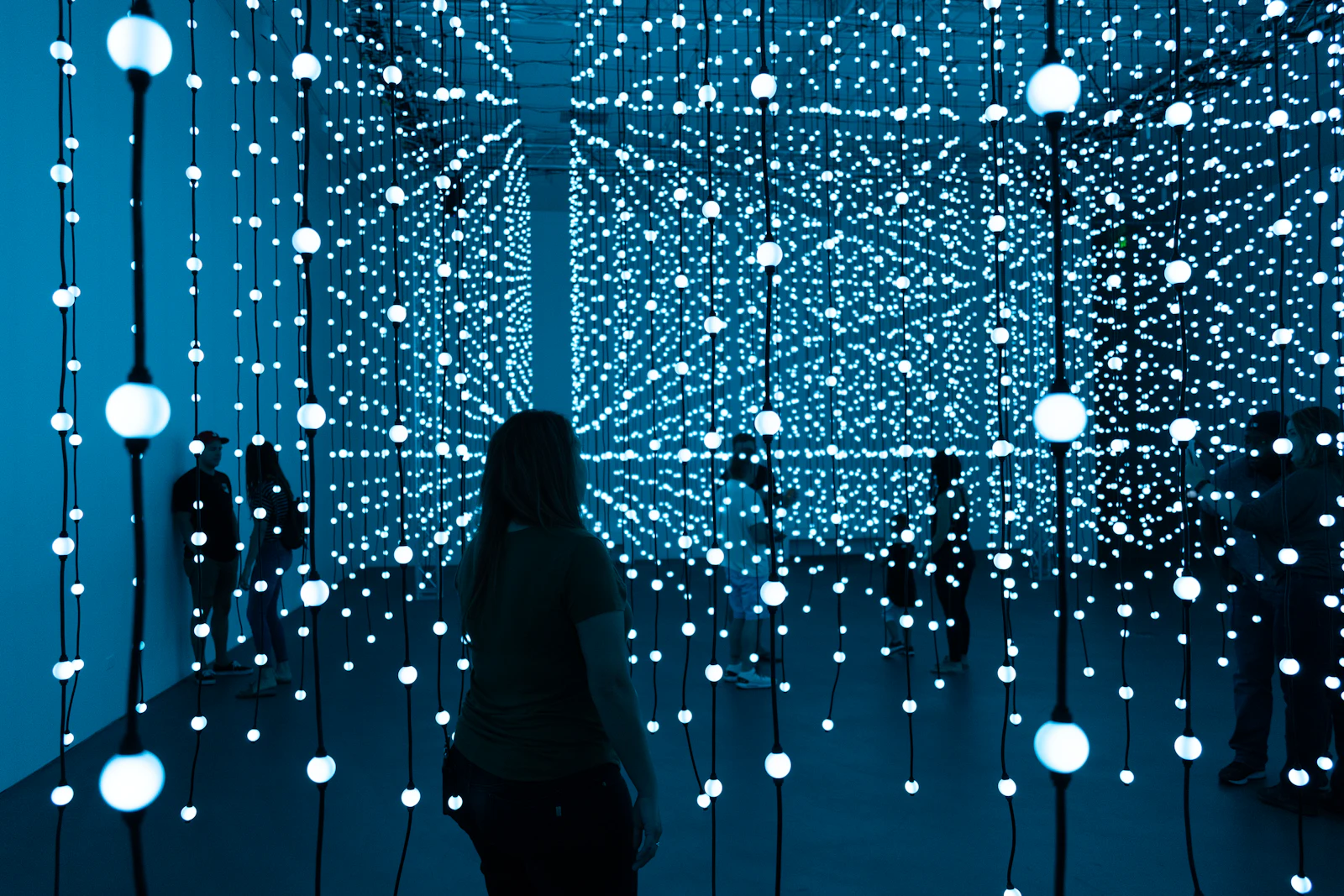 A visitor standing in a dark room filled with hanging points of light