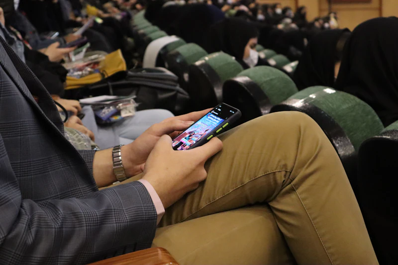 An attendee in an auditorium seat checking an event app on a phone