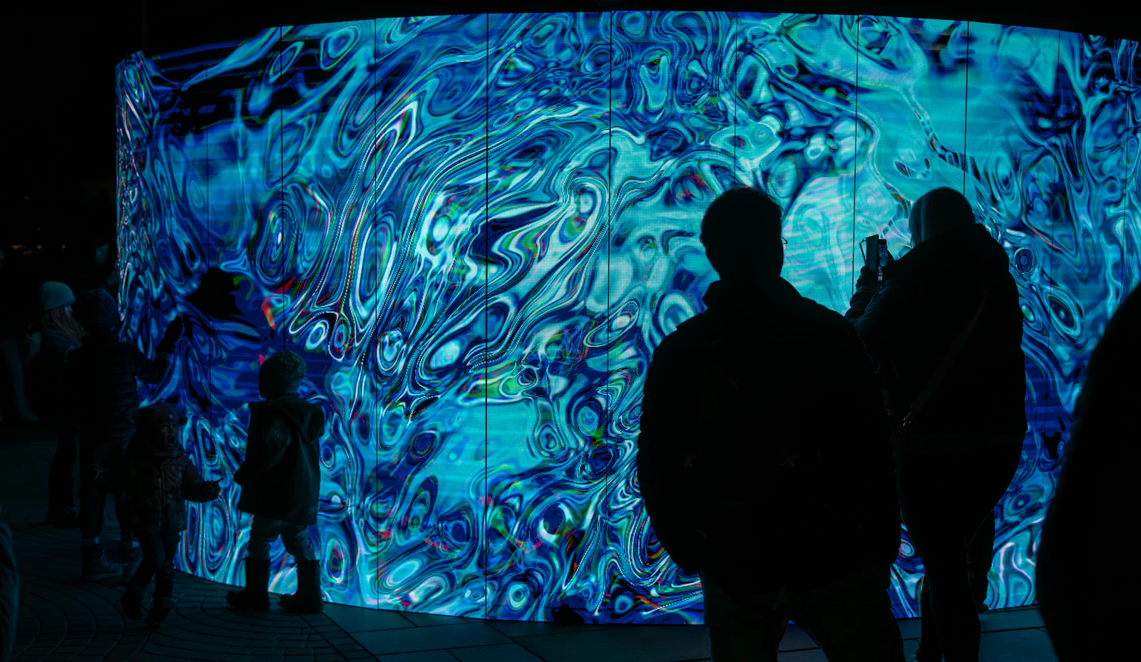 Visitors in silhouette in front of a wall-sized projection of moving blue patterns